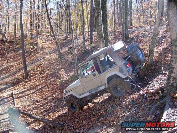 Tan Jeep Wrangler climbing a wooded trail with fallen leaves
