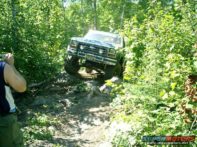 1986 Ford Bronco navigating a rocky, wooded trail