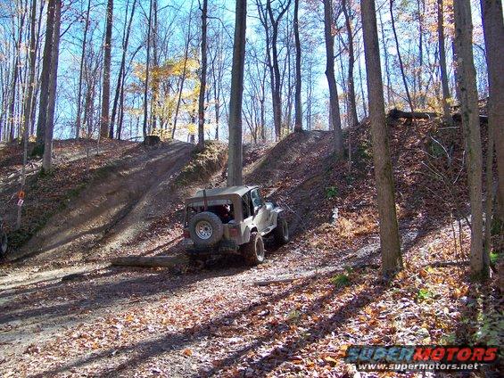 Tan off-road vehicle with spare tire on rear, on dirt path in woods