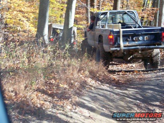 Jeep Comanche pickup truck with roll cage on dirt trail, another vehicle behind it