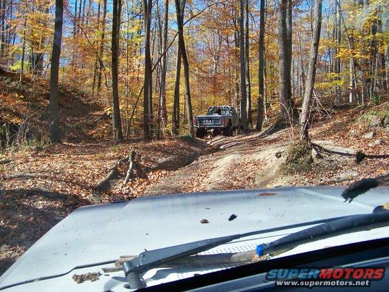 Gray Jeep pickup truck on a dirt trail in an autumn forest