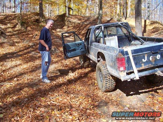 1987 Jeep Comanche pickup truck with door open, parked on a leaf-covered trail