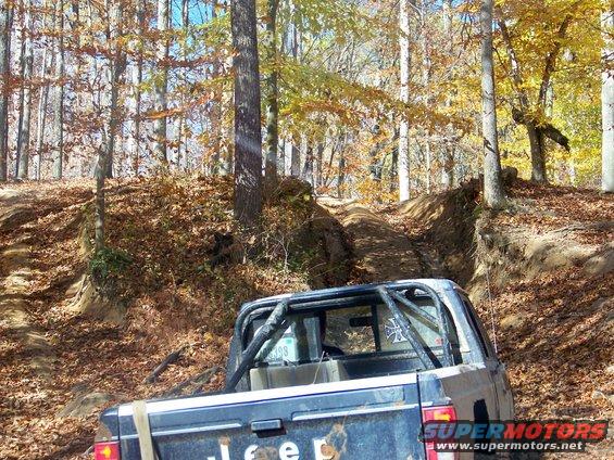 Jeep pickup truck with roll cage on a dirt trail in autumn woods