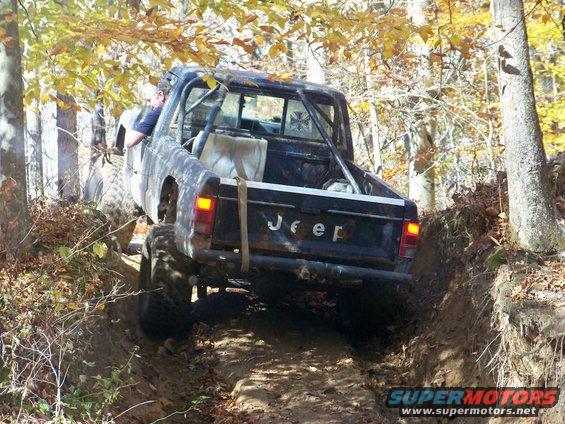 Black Jeep pickup truck with roll cage navigating a steep, muddy trail