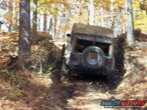 Tan Jeep Wrangler with spare tire on rear, off-roading on a dirt path