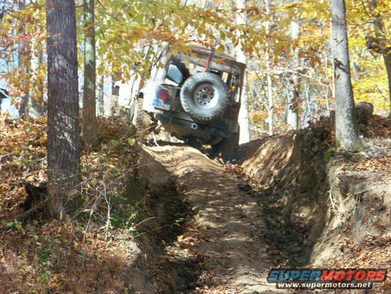 Rear view of a Jeep Wrangler navigating a steep, muddy trail