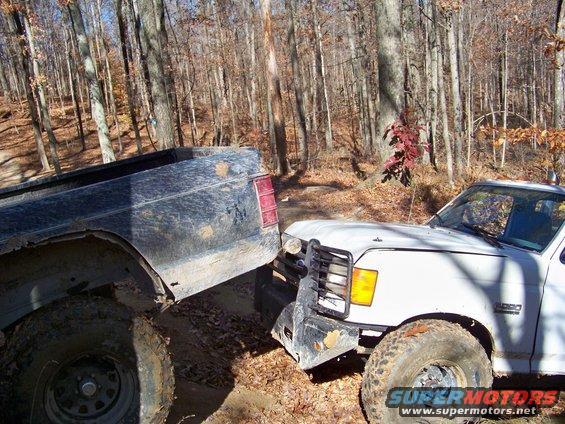 White pickup truck front end, 1990s style grille, off-roading in woods