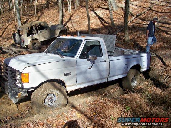 White 1987 Ford F-250 stuck in mud with a Jeep in the background