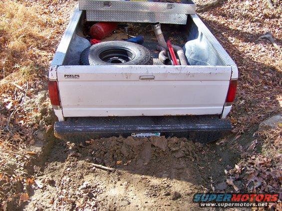 White pickup truck rear stuck in mud, spare tire and toolbox in bed