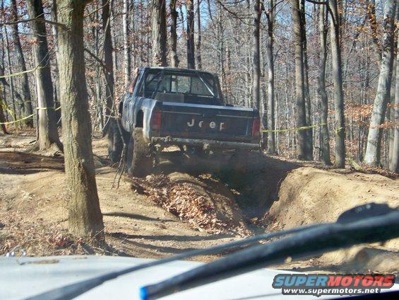 Jeep Comanche pickup truck driving on a dirt trail in woods