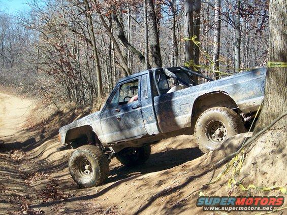 Blue pickup truck with off-road tires climbing a dirt hill, roll cage visible