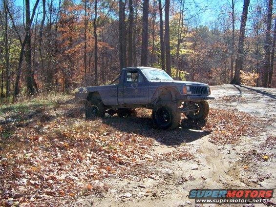 Modified Jeep Comanche pickup truck on a dirt path in the woods