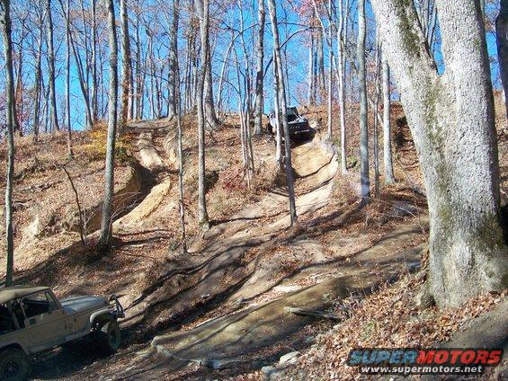 Two off-road vehicles navigate a steep, wooded trail