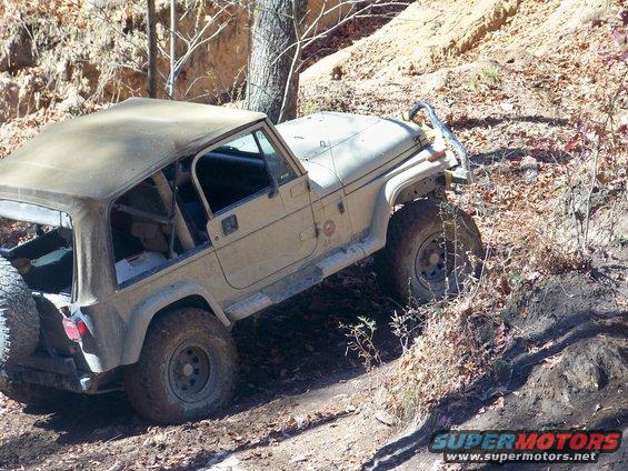 Tan Jeep Wrangler TJ with soft top on a steep, wooded trail