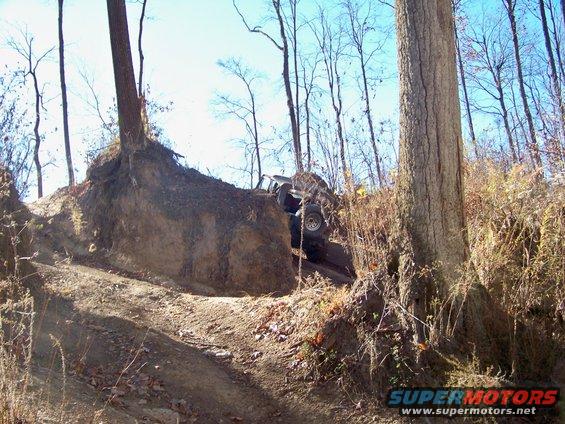 Off-road vehicle climbing a steep, muddy hill next to a large tree