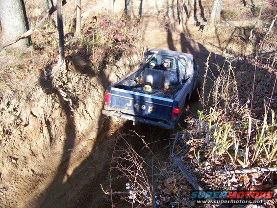 Jeep pickup truck with roll bar driving on a narrow dirt trail in woods