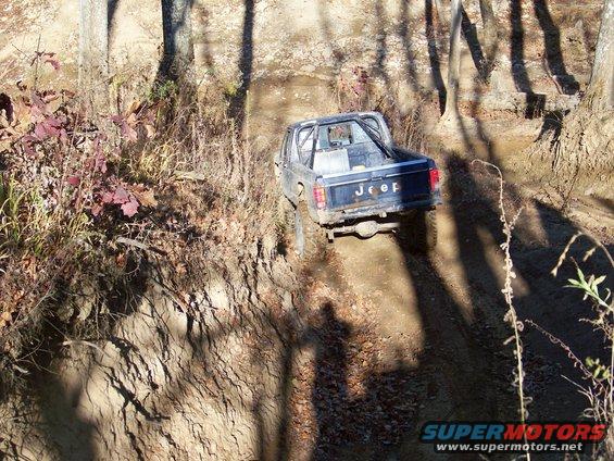 Jeep pickup truck driving on a dirt trail through trees