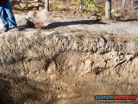 Tire tracks imprinted on a dirt embankment with a person standing nearby