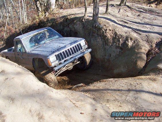 Blue Jeep Comanche pickup truck navigating a steep dirt rut
