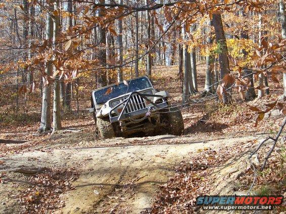 Jeep Wrangler tilted on a dirt trail in a wooded area with fall foliage