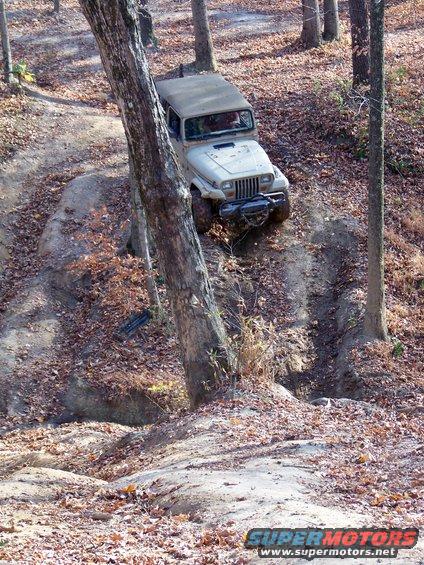 Tan Jeep Wrangler descending a muddy, wooded trail with fallen leaves