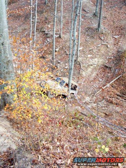 Off-road vehicle on a steep, wooded slope with fall foliage. A winch cable is attached