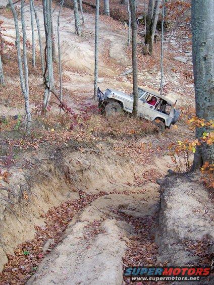 Tan off-road vehicle with red interior on a dirt trail, angled right, with spare tire on rear