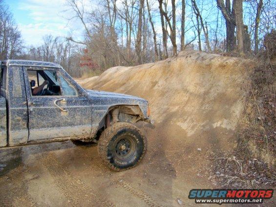 Muddy pickup truck driving on a dirt hill with trees in the background