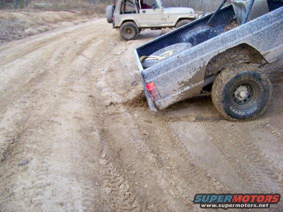 Two off-road vehicles driving on a muddy track with tire ruts
