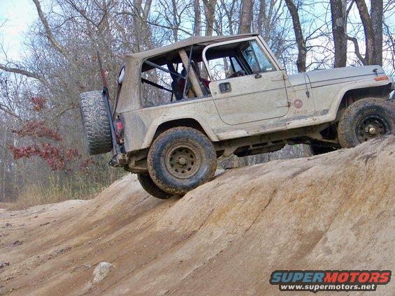 Tan Jeep Wrangler on a rocky incline, spare tire mounted on rear, soft top