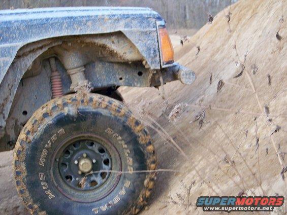 Muddy off-road vehicle side view, front fender and tire visible on sandy terrain