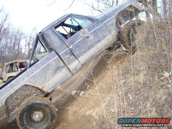 Dark pickup truck tilted on a muddy incline, another SUV visible behind it