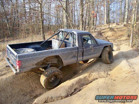 Modified pickup truck with roll cage and large tires on a dirt trail