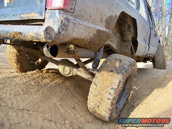 Mud-covered rear axle, leaf springs, and tire of an off-road truck on a dirt track