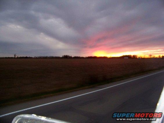 sunset over a field with a road in the foreground