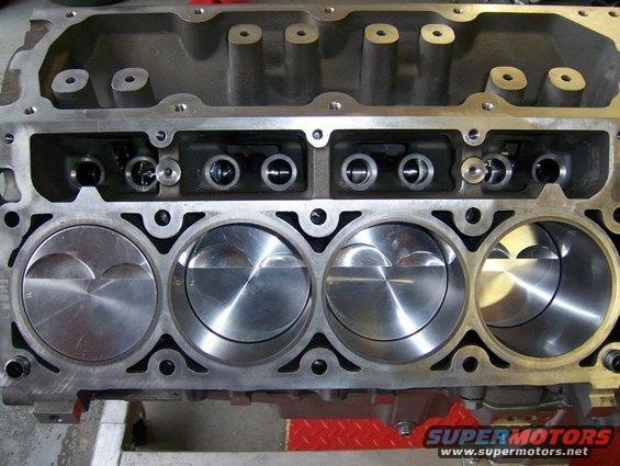 Engine block with four pistons visible in the cylinders. Top of the block shows valve openings