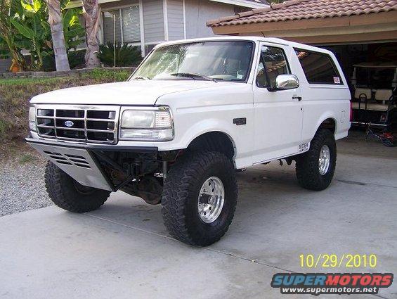White Ford Bronco with aftermarket bumper and large tires, parked in a driveway