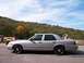 2004 Ford Crown Victoria - A silver 2004 Ford Crown Victoria Police Interceptor is parked on a paved surface with a wooded hill behind it.