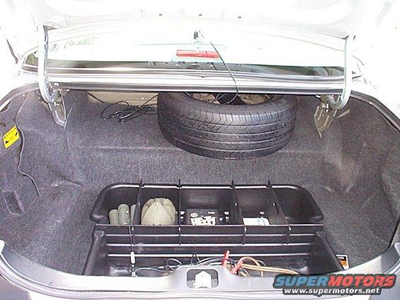 Trunk of a car showing a spare tire, a black organizer with items inside, and some wiring