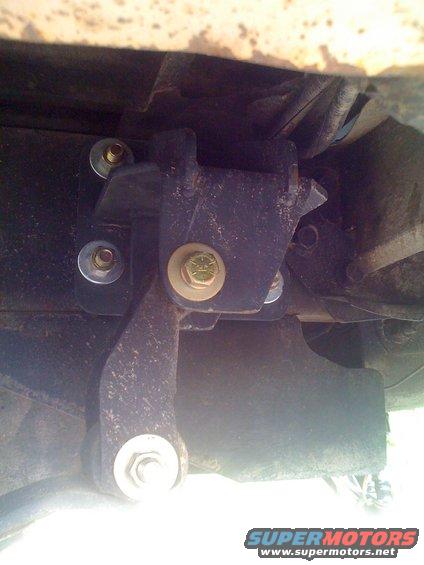 Close-up of a dark metal suspension part with several bolts and washers