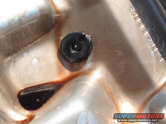 Close-up of a transmission pan with a drain plug and some dark fluid pooled in it