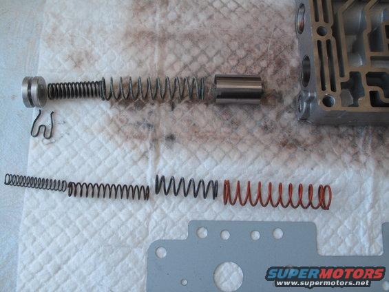 Disassembled transmission valve body components including springs, a plunger, and the valve body itself, on a paper towel. SuperMotors logo visible
