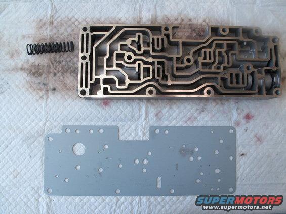Transmission valve body and gasket with a spring on a white cloth. Text reads SUPERMOTORS