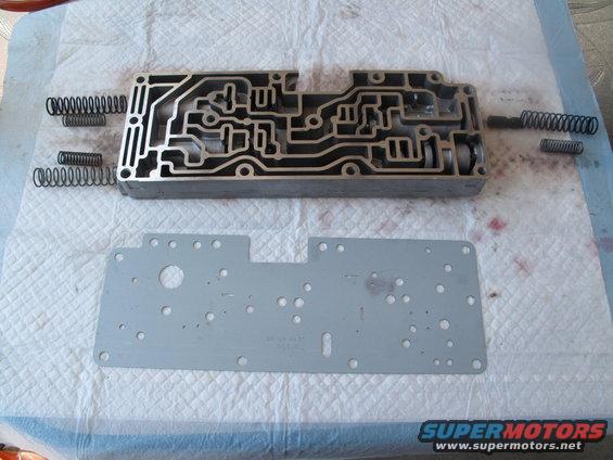 Transmission valve body with internal channels, alongside a metal gasket and several springs
