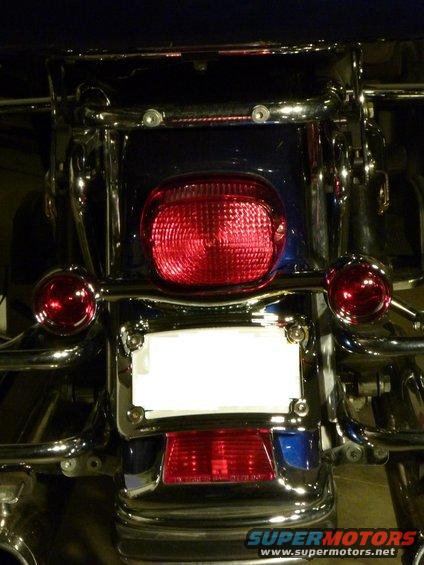 Motorcycle rear with blue bodywork, chrome accents, and a red taillight. Blank license plate area