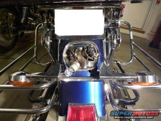Motorcycle rear section with exposed headlight socket and wiring. Another motorcycle is partially visible to the left