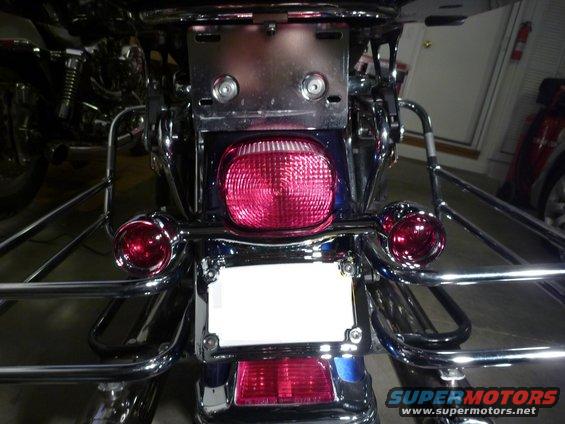 Motorcycle rear with blue bodywork, chrome luggage racks, and a large red taillight. License plate area is blank