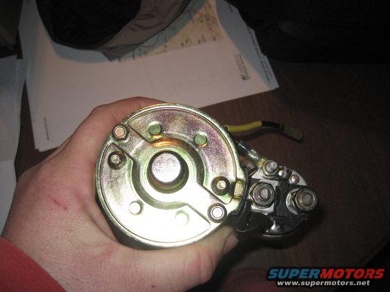Hand holding a starter motor with yellow and black wires attached