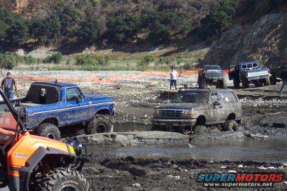 Mud-covered blue 1978 Ford Bronco with large tires stuck in mud