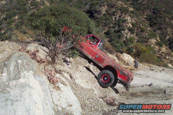 Red off-road truck tilted on a rocky incline, driver visible inside